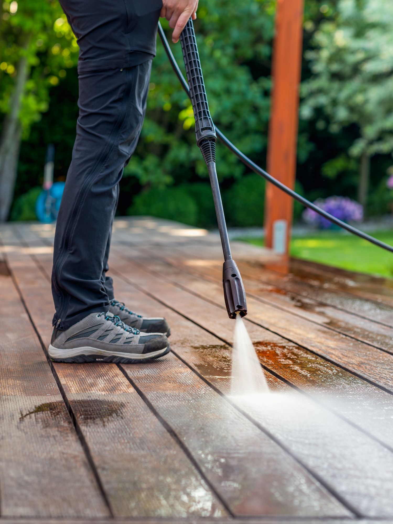 Person using a pressure washer to clean a wooden deck outdoors.