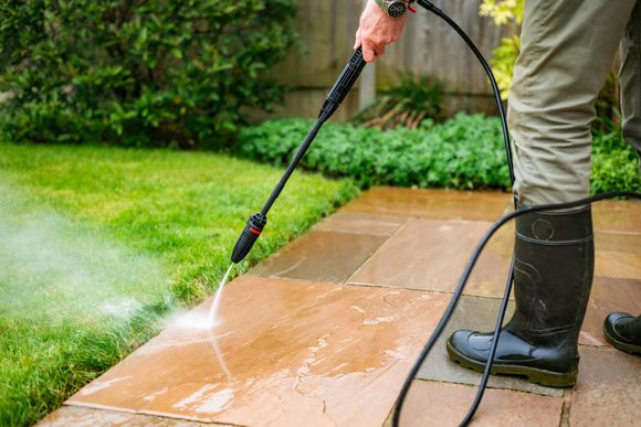 Person pressure washing a stone patio in a backyard, spray water and steam.