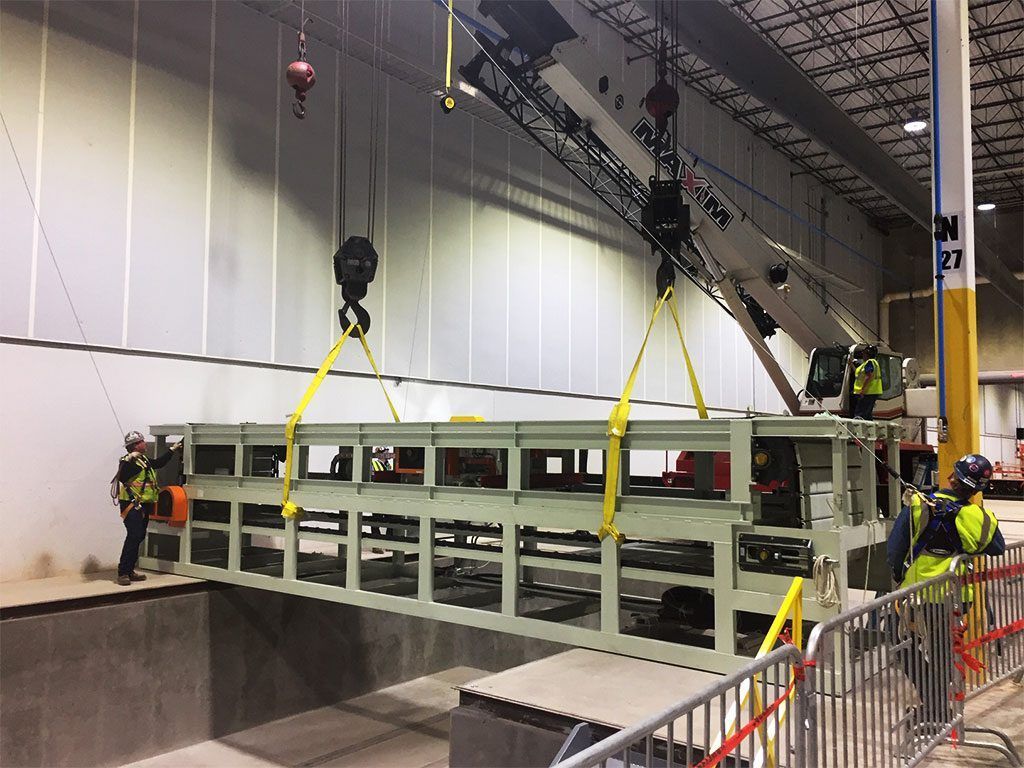 Crane lifting a large, rectangular industrial machine into a recessed area within a warehouse