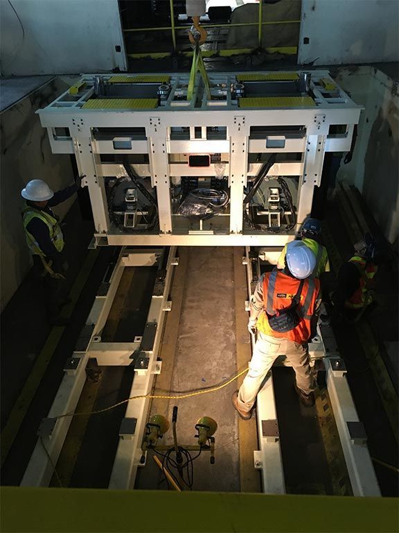 Workers install a large white metal machine component in an industrial setting.