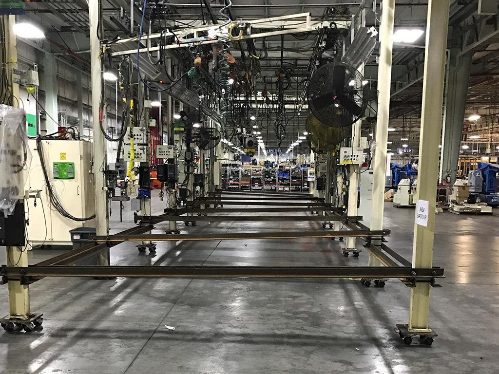 Assembly line in a factory. Empty metal frames on wheels on the floor. Overhead equipment and supports.