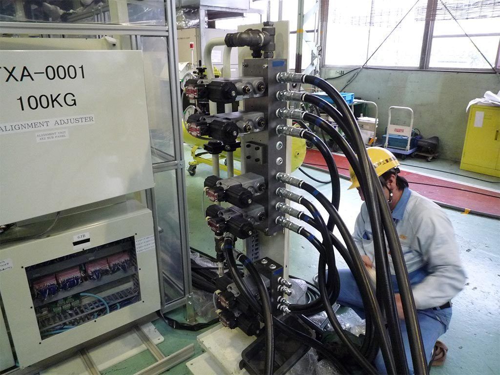 A person wearing a hard hat working on machinery with many black tubes. White cabinet on the left.