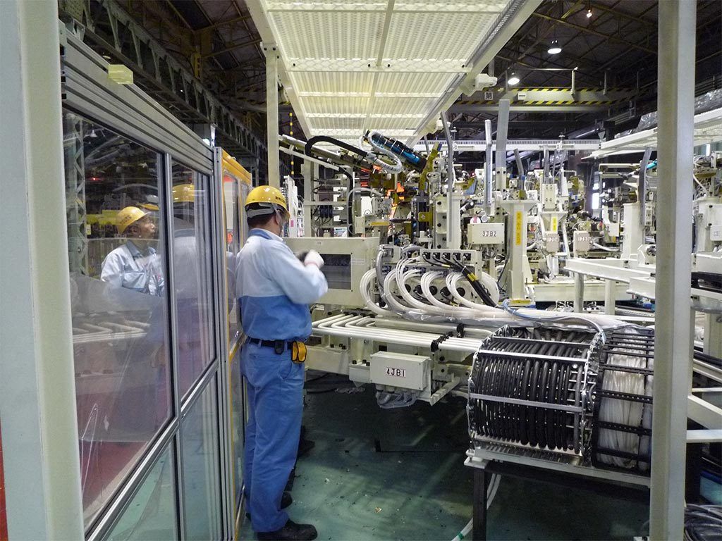 Factory worker in blue uniform inspects automated machinery. Factory interior, bright lighting, machinery components.