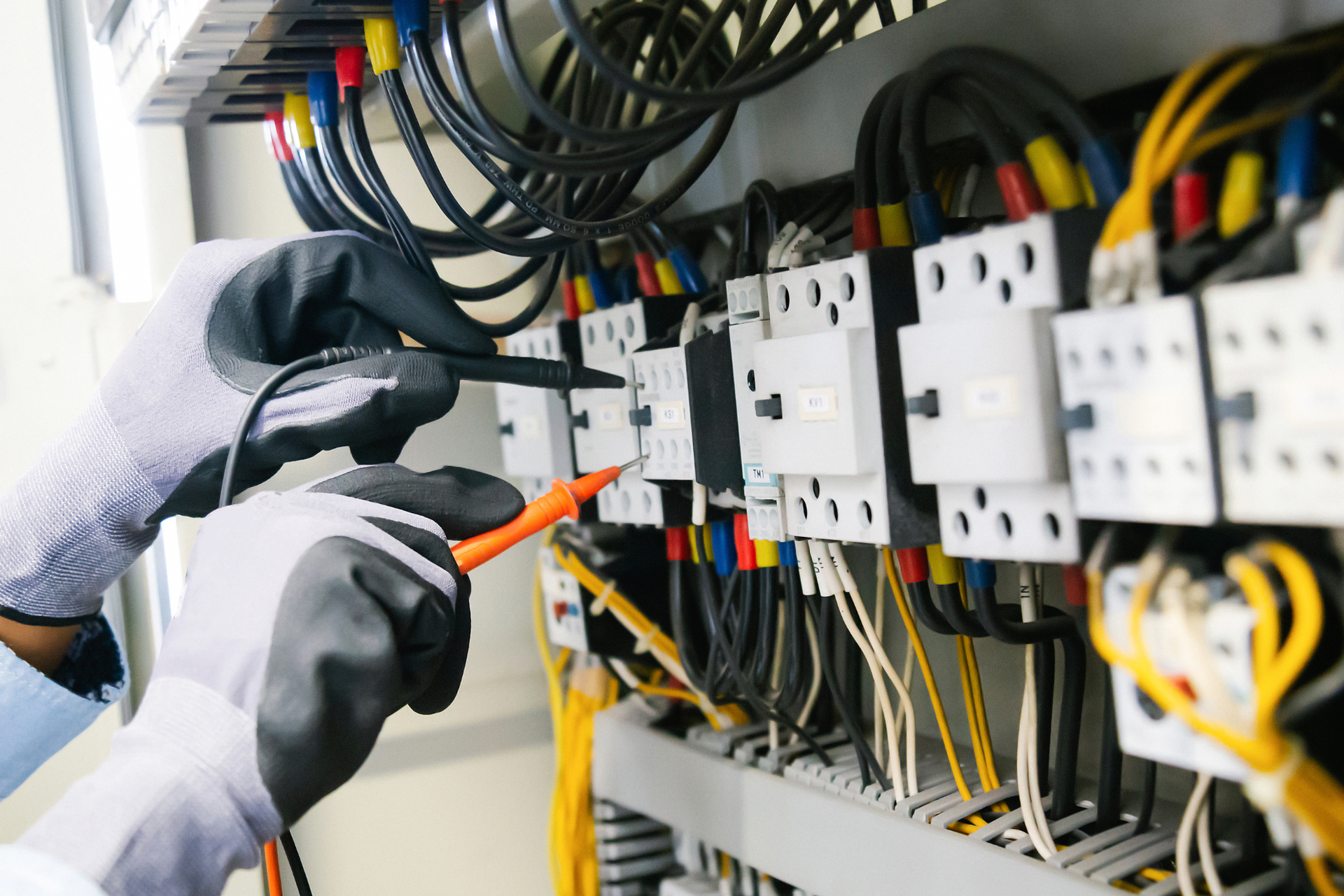 Electrician in gloves testing wires in a panel with multicolored wires.