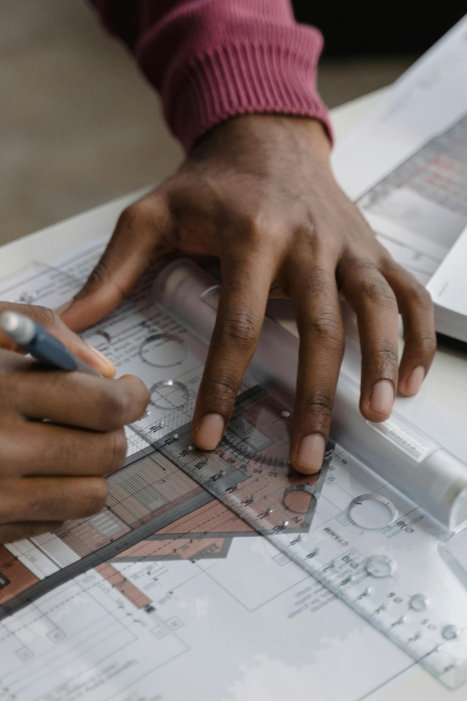Person's hands using a ruler and pen to draw on architectural blueprints.