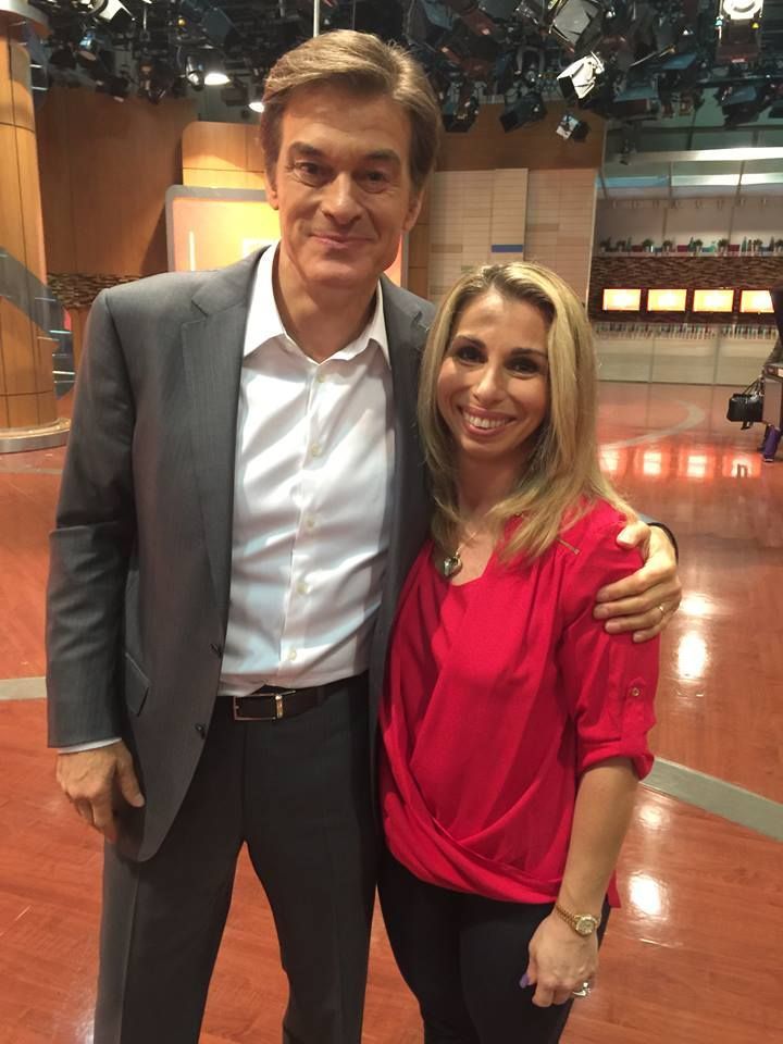 Dr. Oz with a woman on a television set. They are smiling, and he has his arm around her.