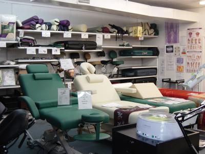 A showroom with massage chairs and tables in varying colors displayed on the floor and shelves.