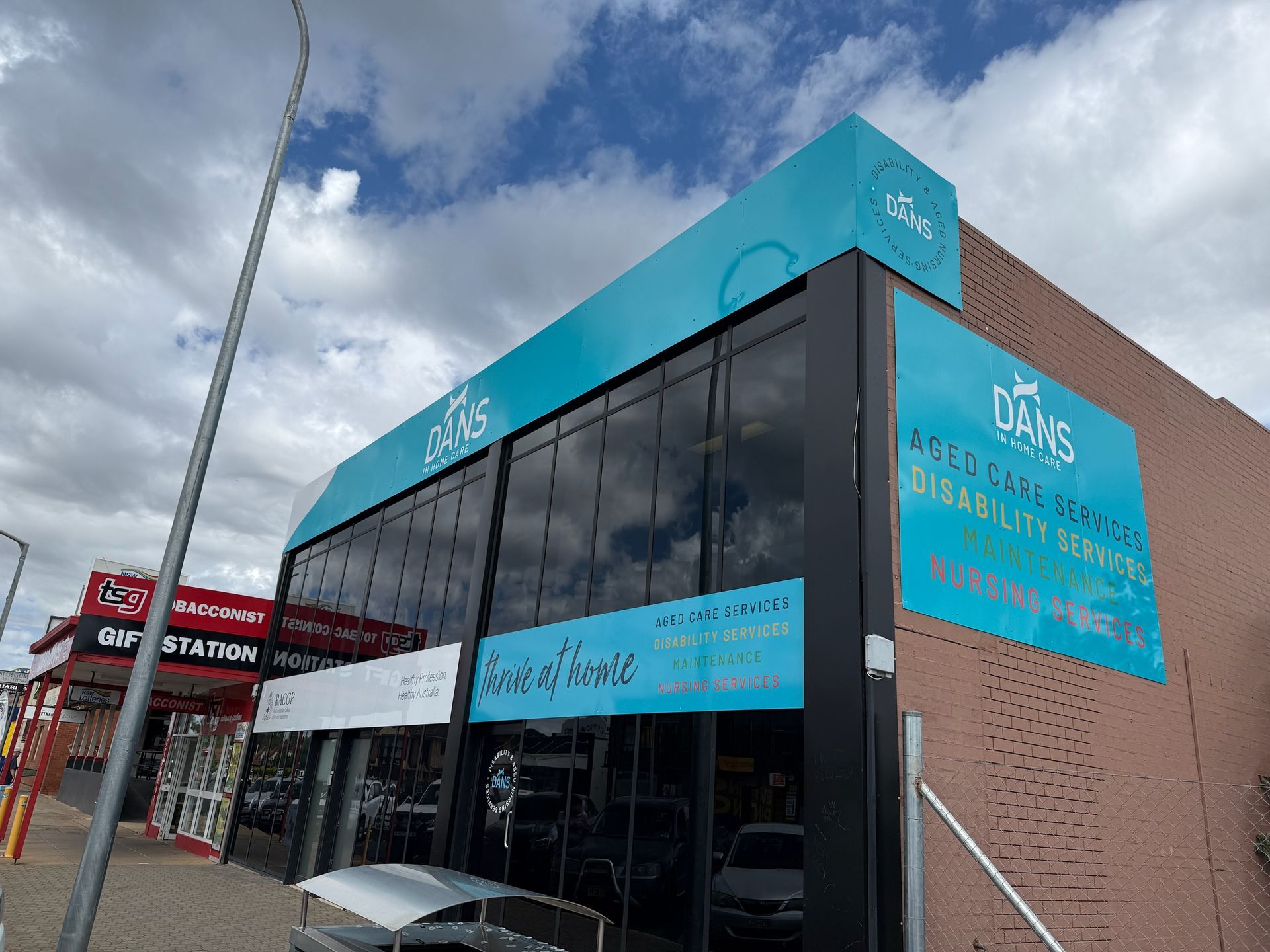 Exterior of DAKS building with teal signage; brick wall and large glass windows.