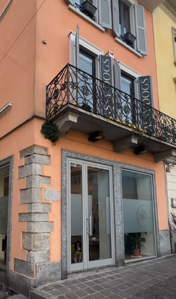 Facciata arancione dell'edificio con vetrina, piccolo balcone con ringhiera nera e finiture in pietra all'angolo.