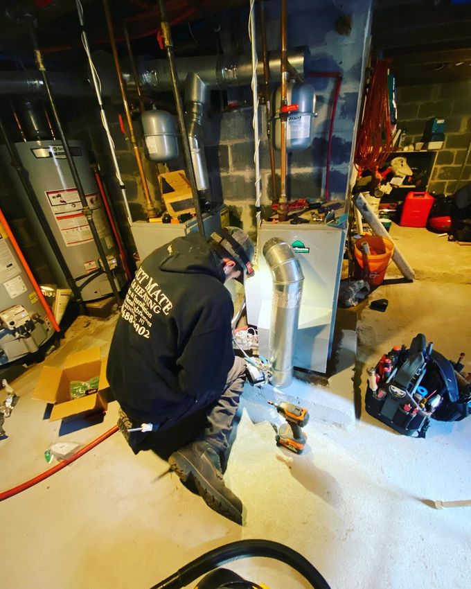 Worker kneeling in a basement utility room, inspecting HVAC equipment and pipes near exposed ducts. Worker kneeling in a basement utility room, inspecting HVAC equipment and pipes near exposed ducts.