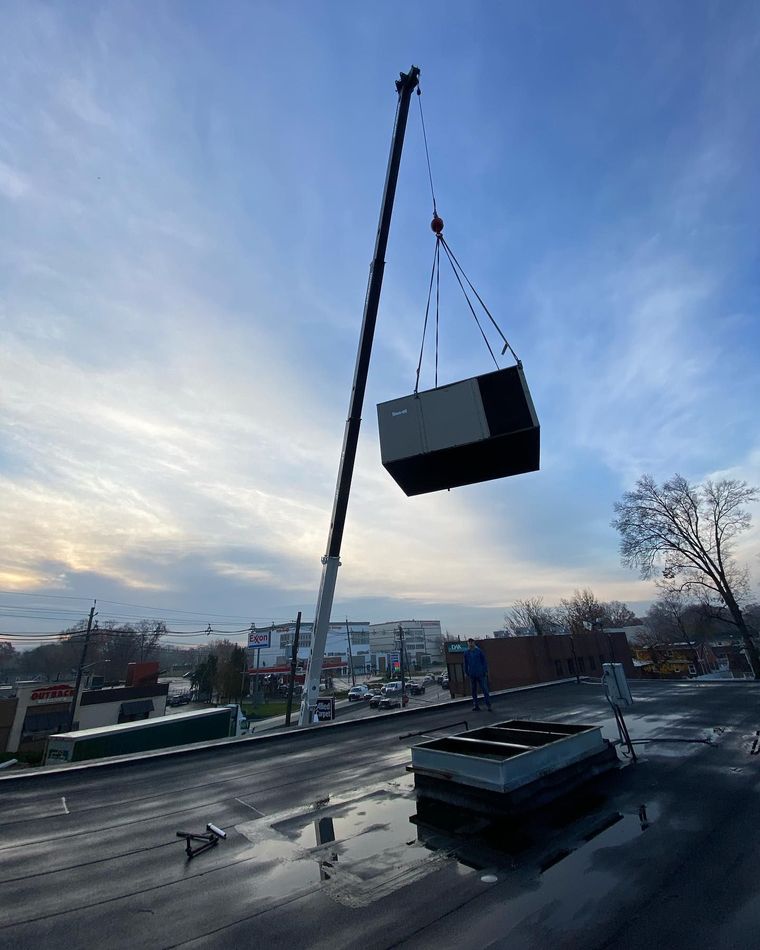 Crane lifting a large black container over a rooftop at dusk under a blue sky Crane lifting a large black container over a rooftop at dusk under a blue sky