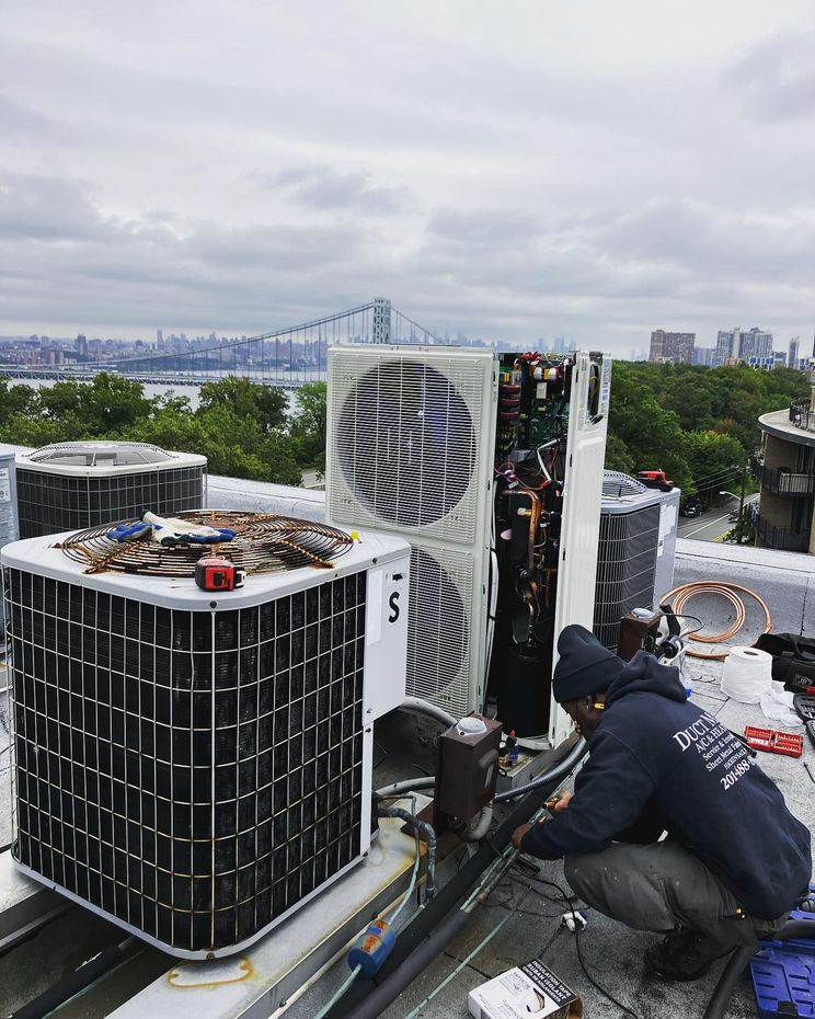 Technicians repairing rooftop HVAC units with a city skyline and bridge in the background Technicians repairing rooftop HVAC units with a city skyline and bridge in the background