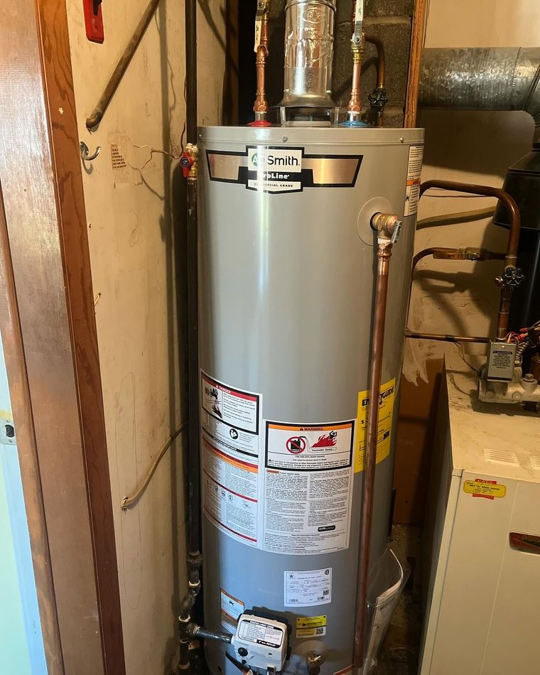 Tall silver water heater in a basement utility area with pipes and labels attached Tall silver water heater in a basement utility area with pipes and labels attached