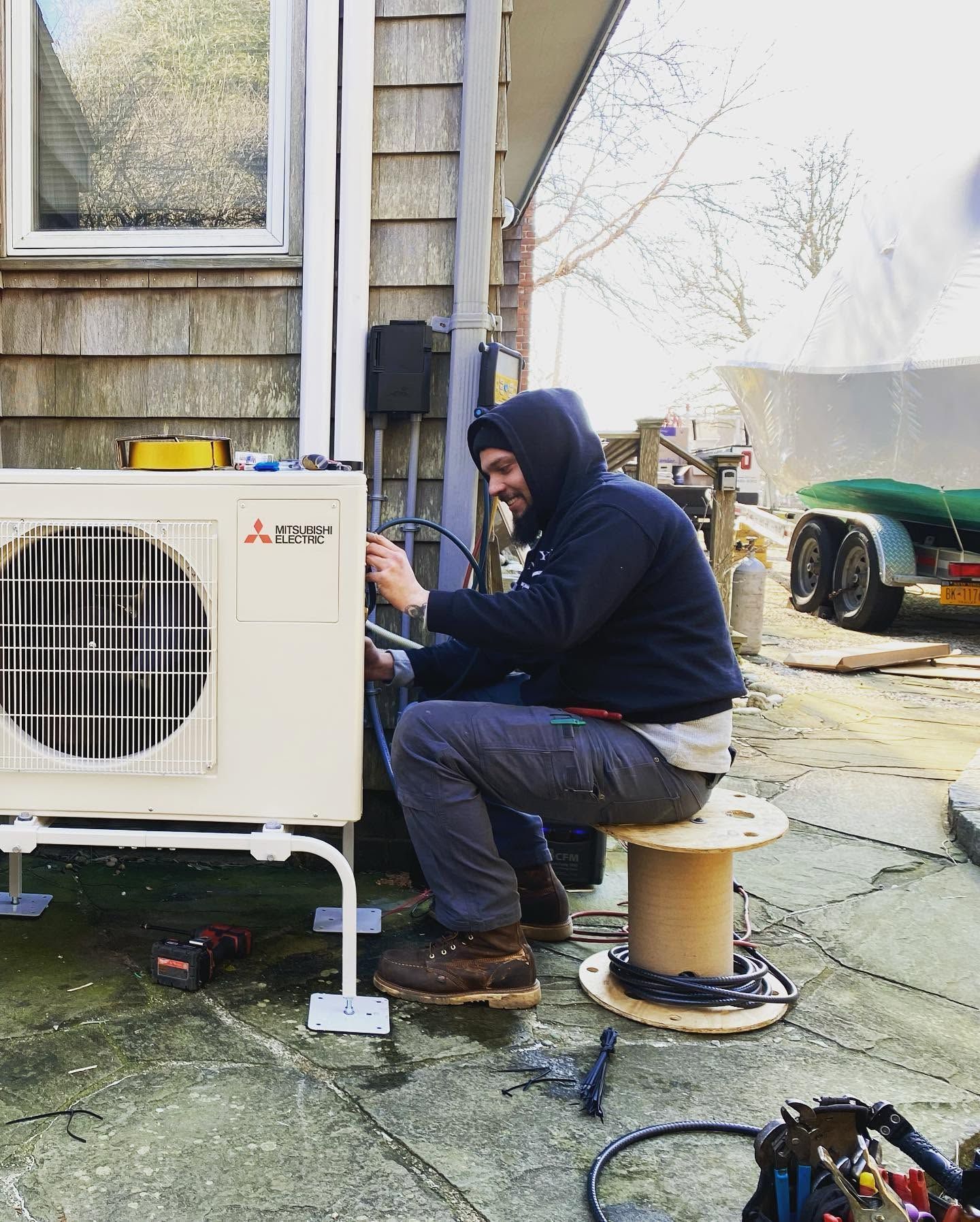 Technician kneels beside an outdoor HVAC unit at a house, inspecting or repairing it. Technician kneels beside an outdoor HVAC unit at a house, inspecting or repairing it.
