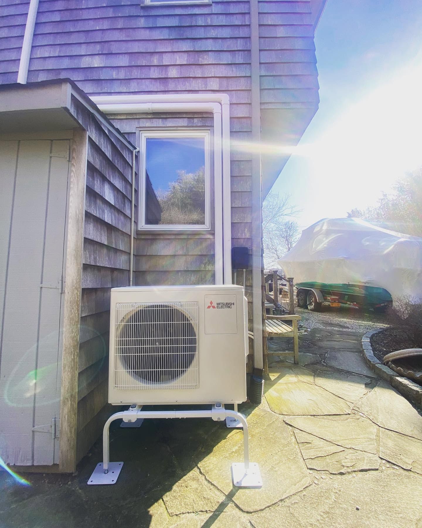 Outdoor HVAC unit beside a house, with bright sun glare and a stone patio in the foreground Outdoor HVAC unit beside a house, with bright sun glare and a stone patio in the foreground