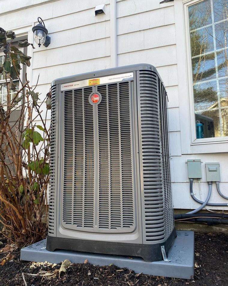 Outdoor HVAC unit beside a house wall, with white siding and a nearby window. Outdoor HVAC unit beside a house wall, with white siding and a nearby window.