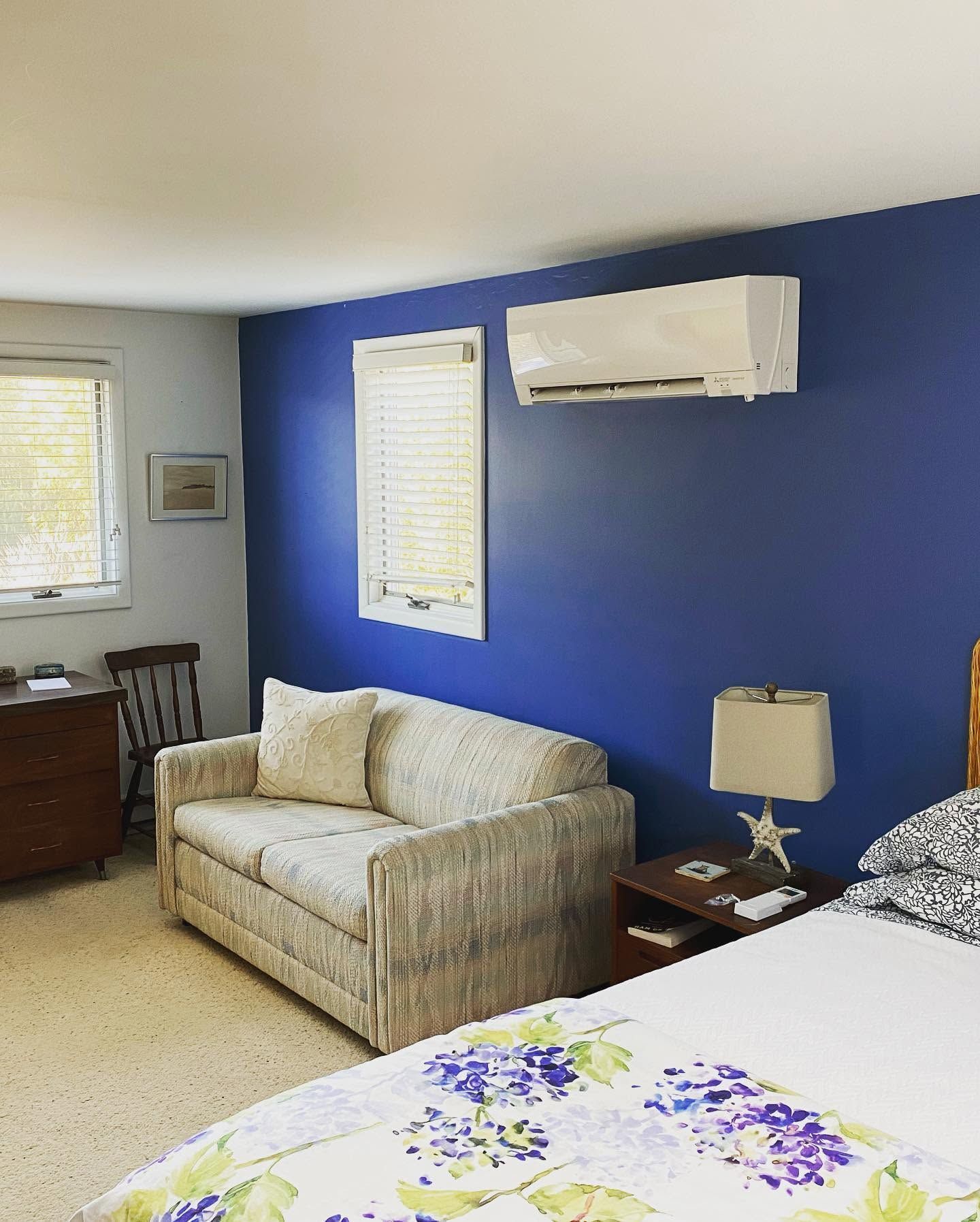 Bedroom with blue accent wall, bed, sofa, window, and wall-mounted air conditioner Bedroom with blue accent wall, bed, sofa, window, and wall-mounted air conditioner