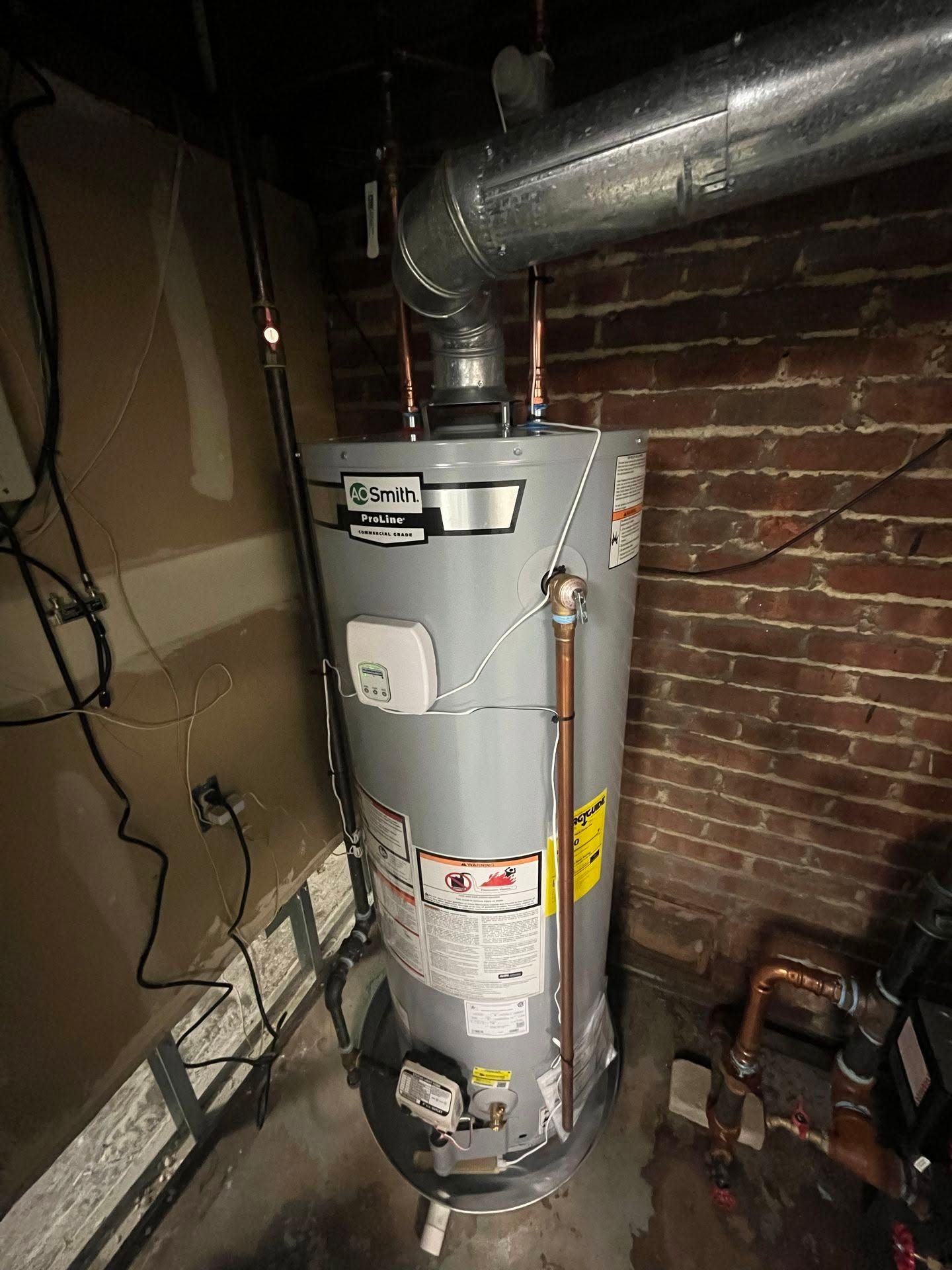 Basement water heater with metal ductwork beside a brick wall and exposed pipes Basement water heater with metal ductwork beside a brick wall and exposed pipes