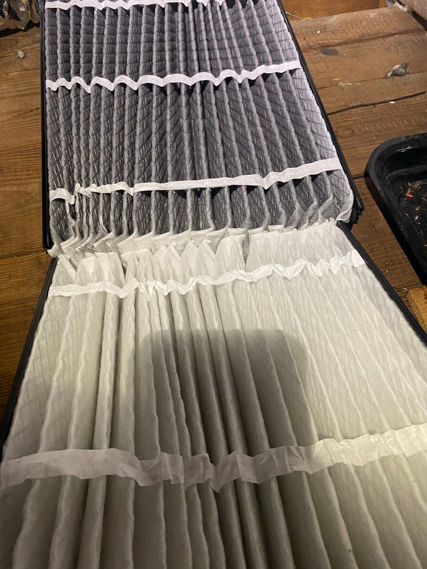 Opened pleated accordion-style filter with gray and white pleats on a wooden surface Opened pleated accordion-style filter with gray and white pleats on a wooden surface