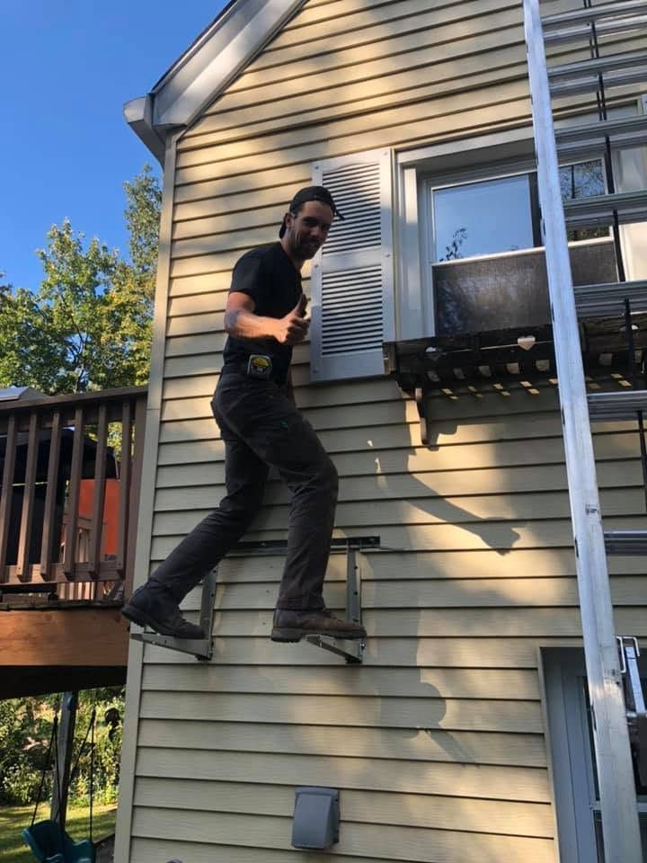 Person climbing a house wall near a window and deck, wearing black clothes and safety boots Person climbing a house wall near a window and deck, wearing black clothes and safety boots