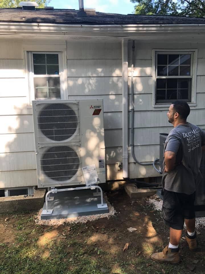 Outdoor HVAC unit beside a house; a man stands nearby inspecting it. Outdoor HVAC unit beside a house; a man stands nearby inspecting it.