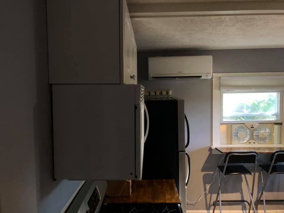 Small apartment kitchen and dining nook with gray cabinets, black fridge, table, chairs, and window air conditioner Small apartment kitchen and dining nook with gray cabinets, black fridge, table, chairs, and window air conditioner