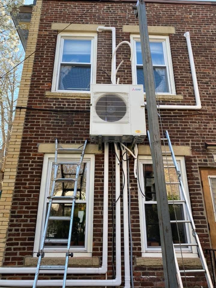 Brick building facade with windows, exterior AC unit, and several pipes and ladders attached to the wall. Brick building facade with windows, exterior AC unit, and several pipes and ladders attached to the wall.