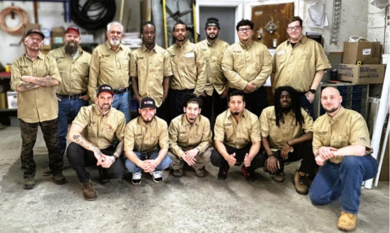 Group of workers in tan uniforms posing in a warehouse, some standing and some kneeling. Group of workers in tan uniforms posing in a warehouse, some standing and some kneeling.