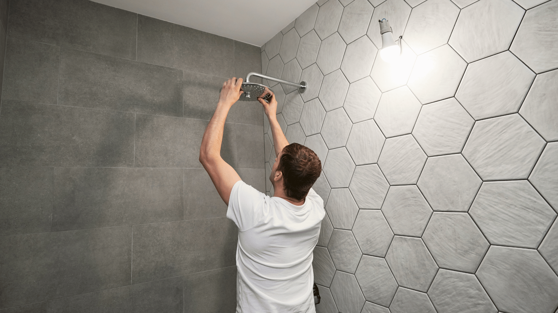A man is installing a shower head in a bathroom.