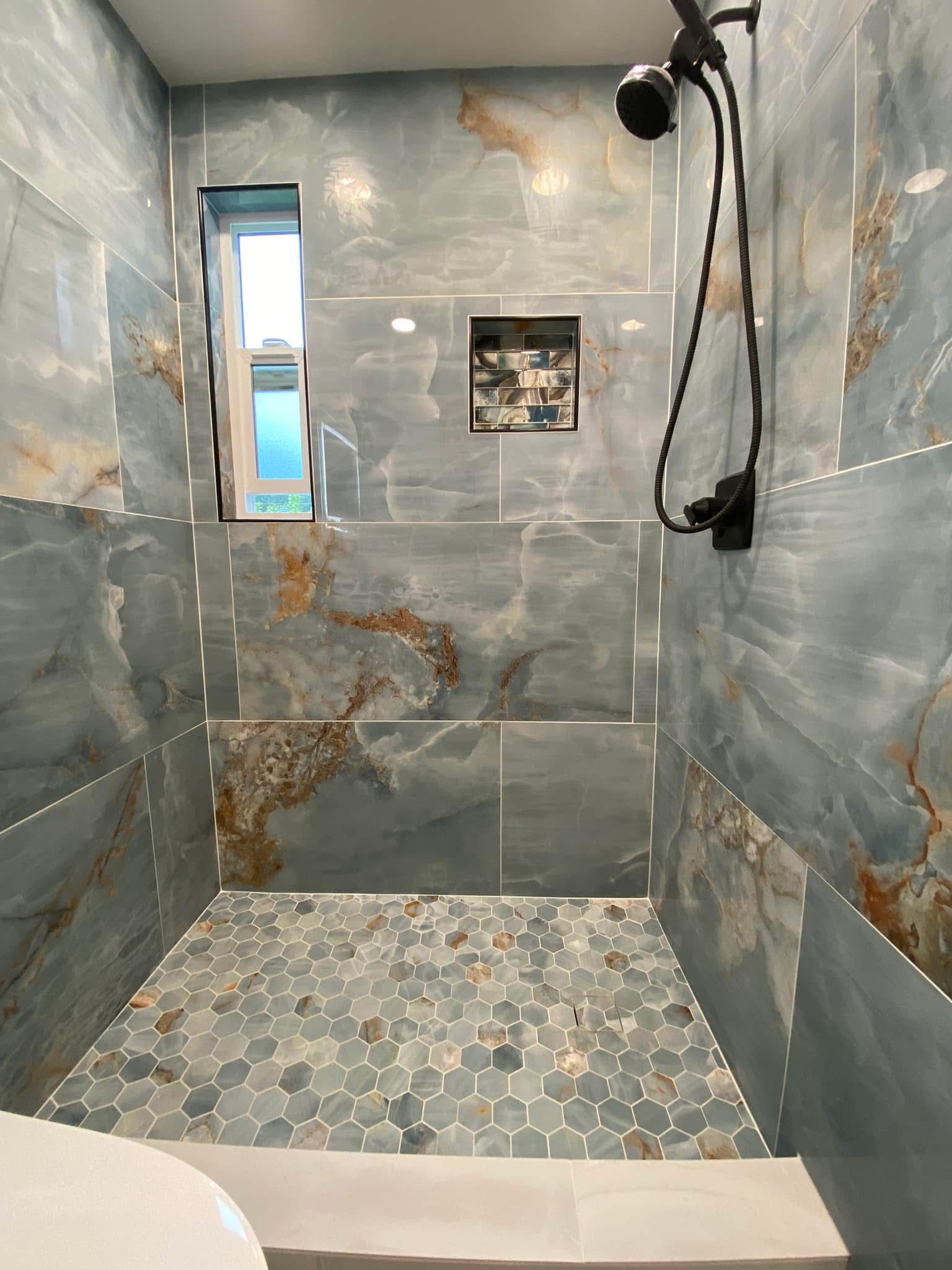 Blue-tiled shower with a mosaic floor, a small window, and a black showerhead.