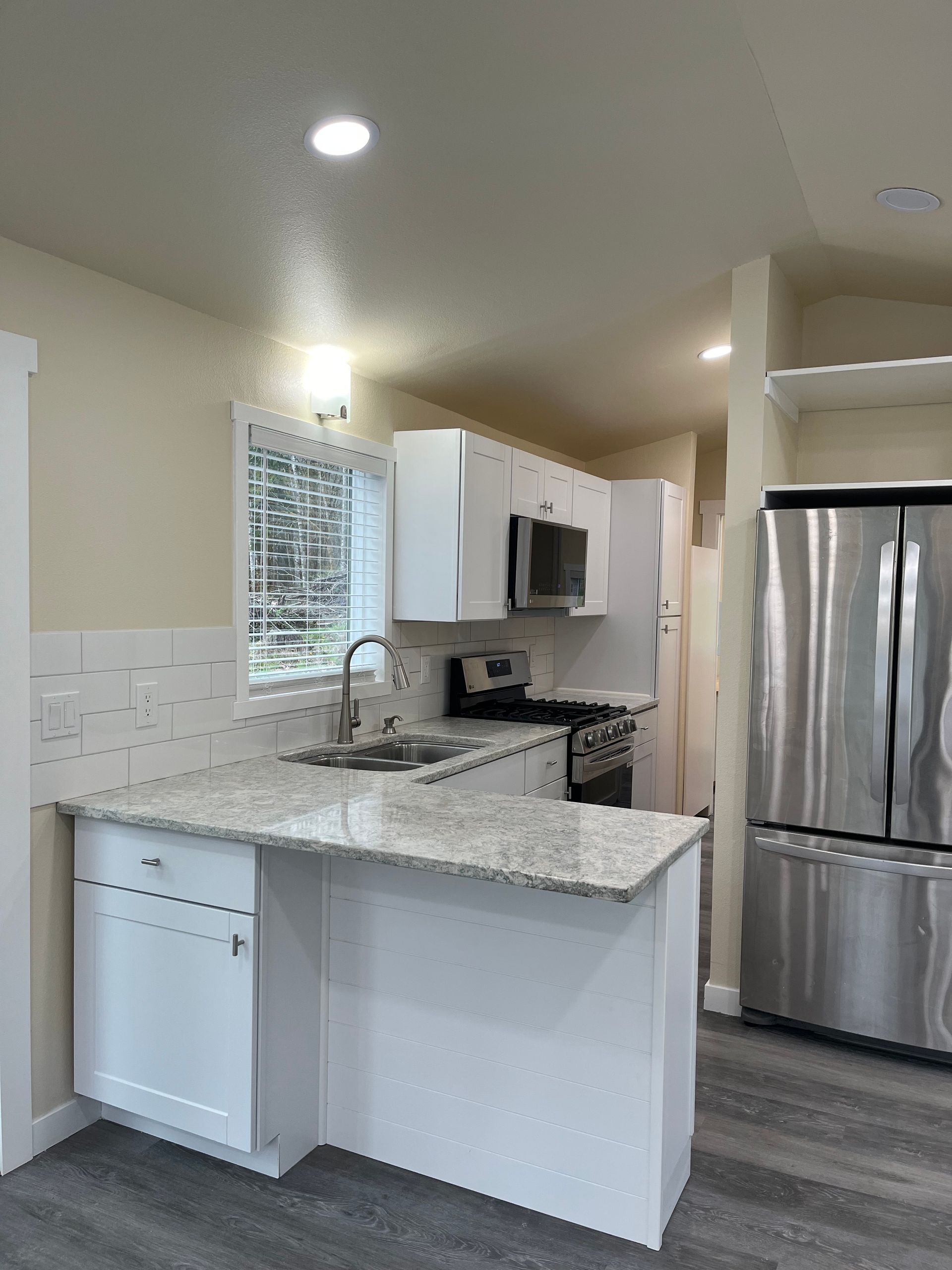 Modern white kitchen with granite countertops, stainless steel appliances, and gray flooring.