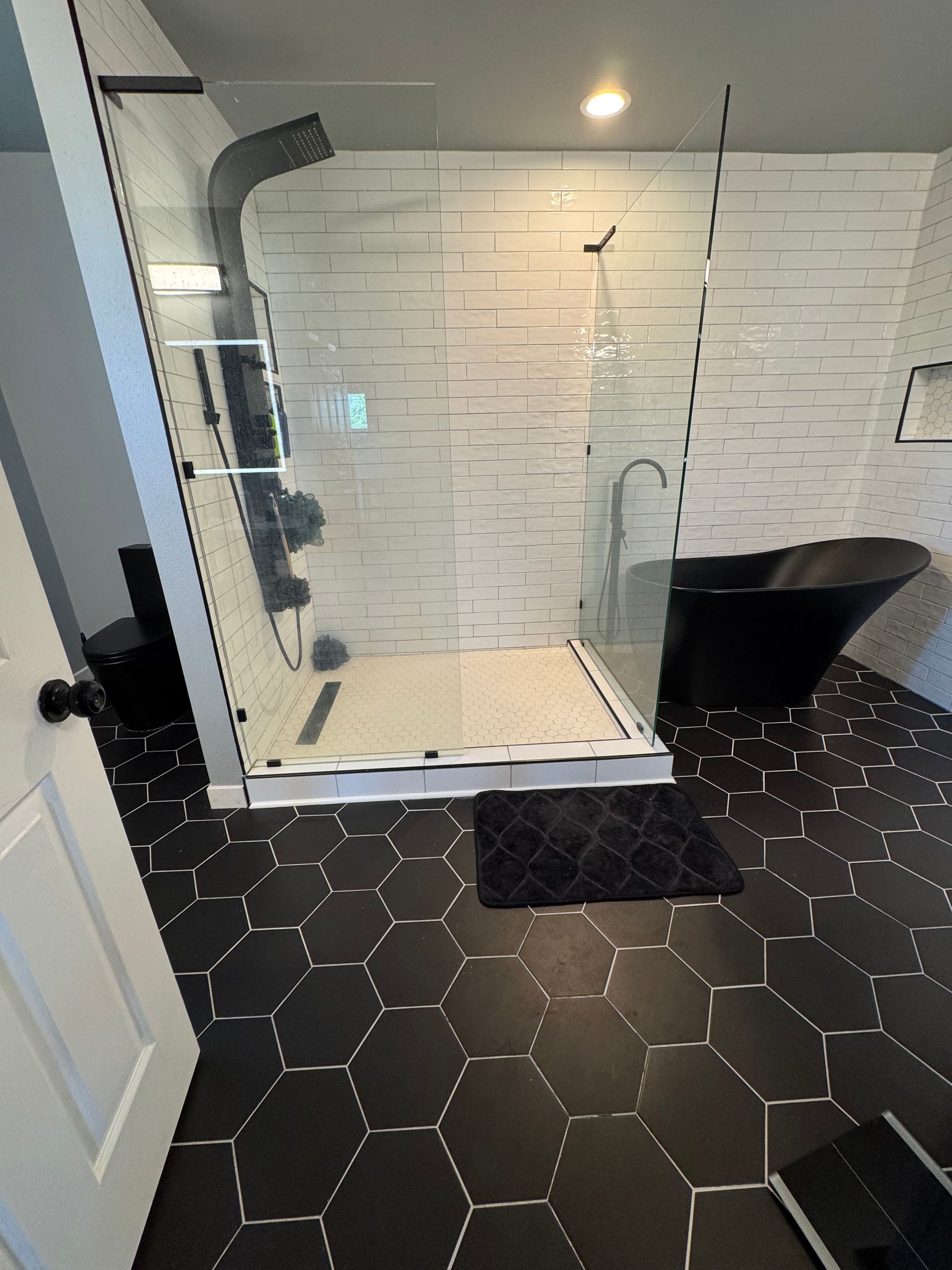 Modern black and white bathroom with a glass shower, black tub, and geometric tile flooring.