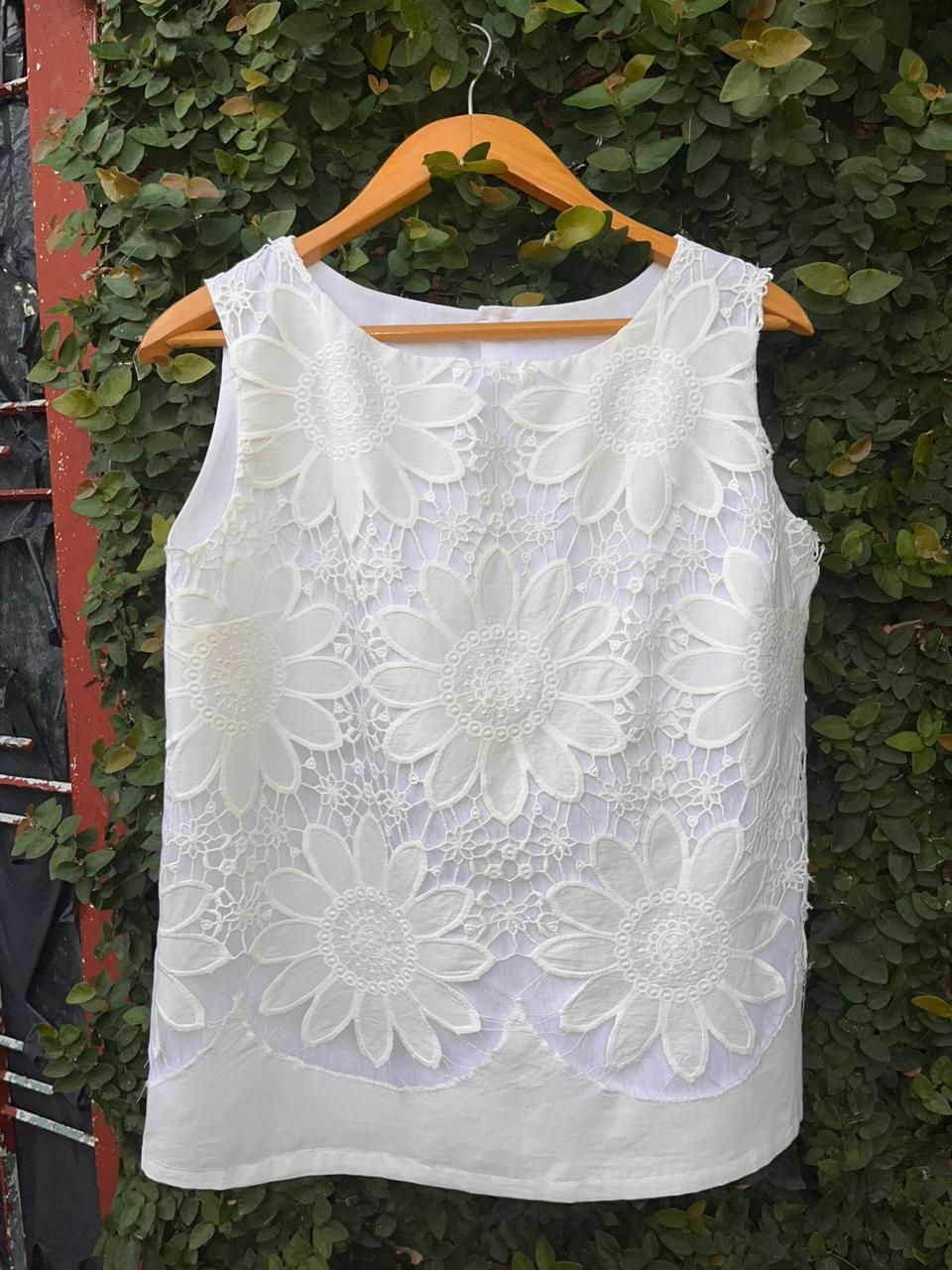 Un top de encaje blanco cuelga de una percha de madera.