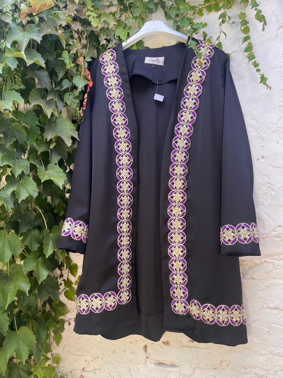 Una chaqueta negra con bordado morado está colgada en una percha.