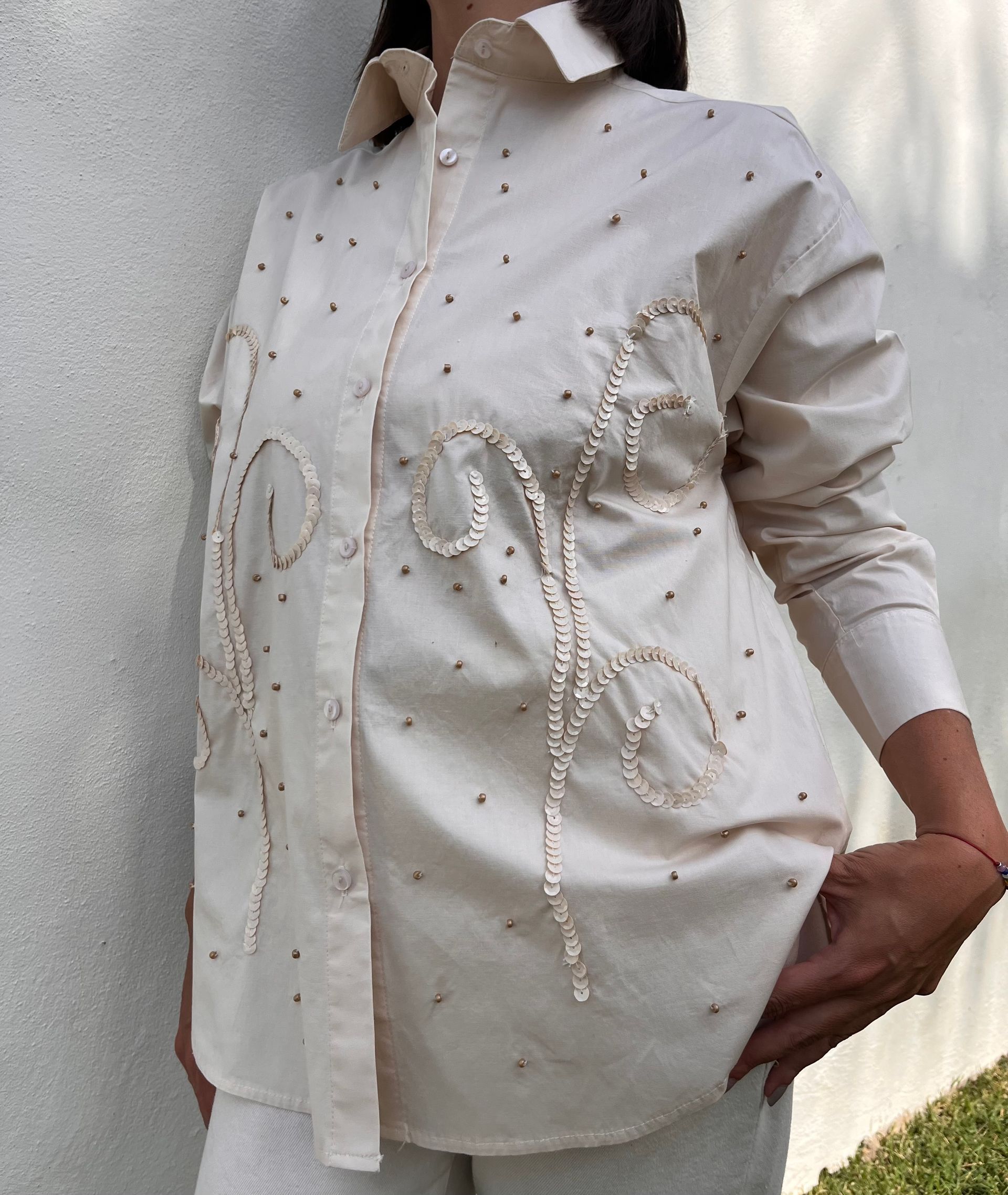 Una mujer lleva una camisa blanca con perlas.