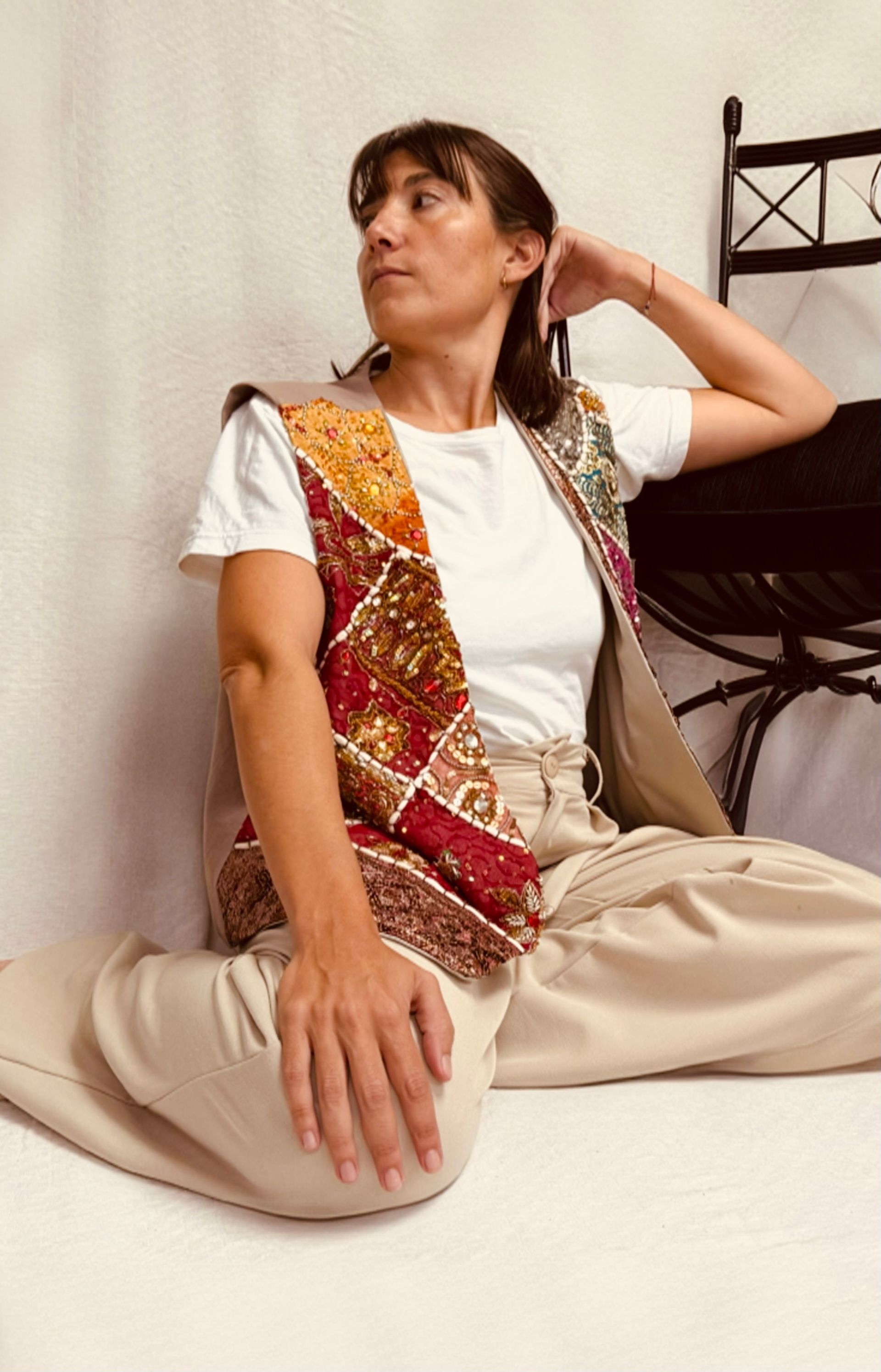 Una mujer está sentada en el suelo vistiendo un chaleco y una camiseta blanca.