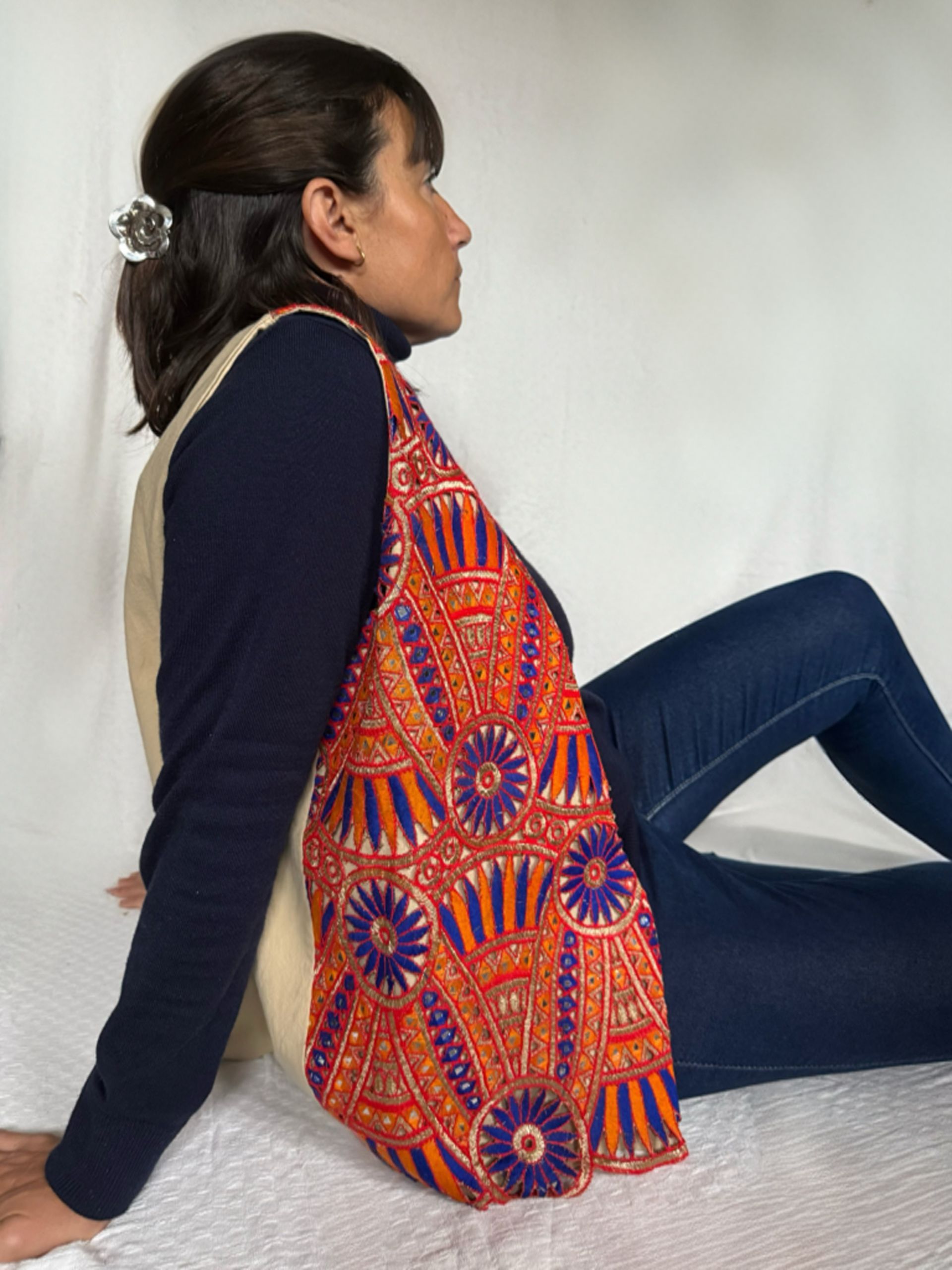 Una mujer está sentada en el suelo vistiendo un chaleco colorido.