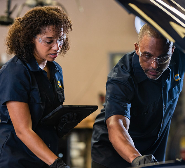 Two people in auto shop uniforms inspecting a car engine | AUTOPRO Oakville