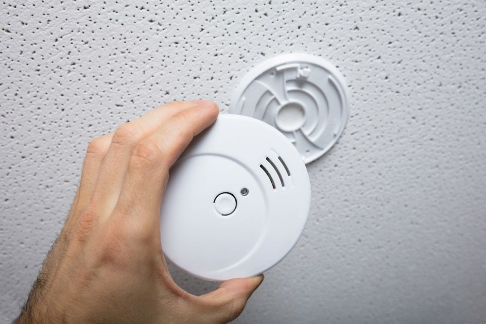 Hand Attaching a White Smoke Detector to a Textured Ceiling — FNQ Smoke Alarms & Maintenance in Malanda, QLD