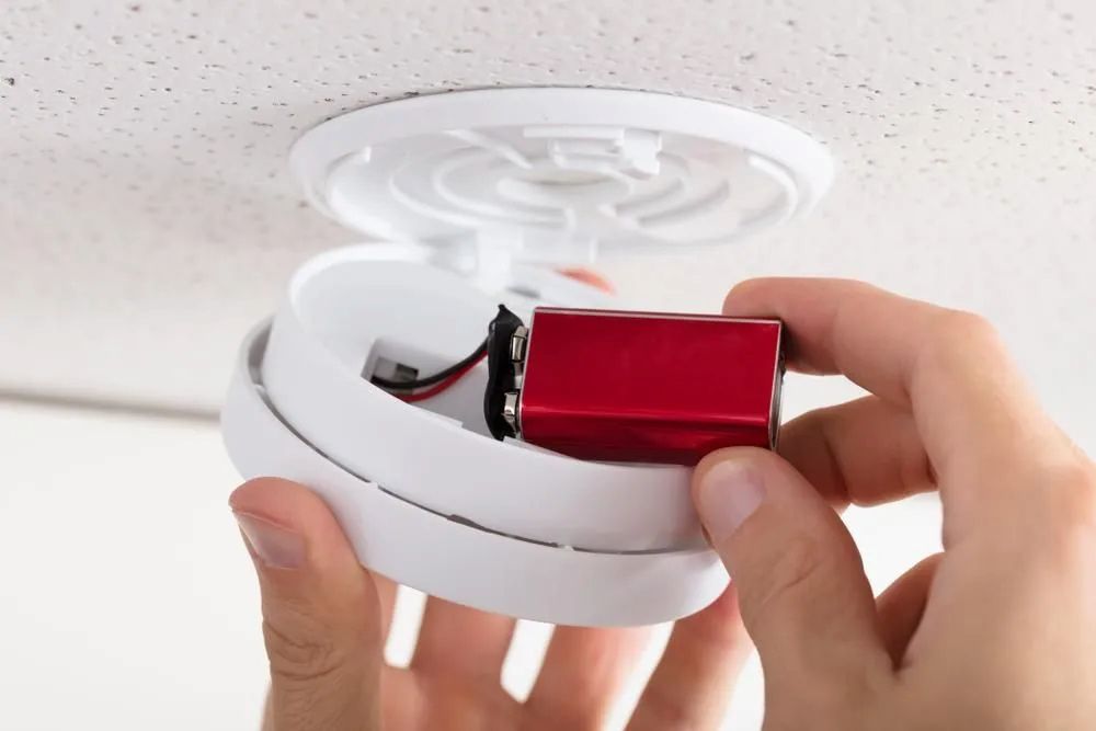 Person Replacing a Red 9-volt Battery in a White Smoke Detector — FNQ Smoke Alarms & Maintenance in Goldsborough, QLD
