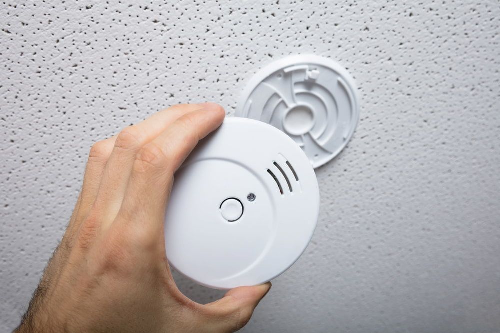 Hand Installing a White Smoke Detector Onto a Textured Ceiling — FNQ Smoke Alarms & Maintenance in Goldsborough, QLD