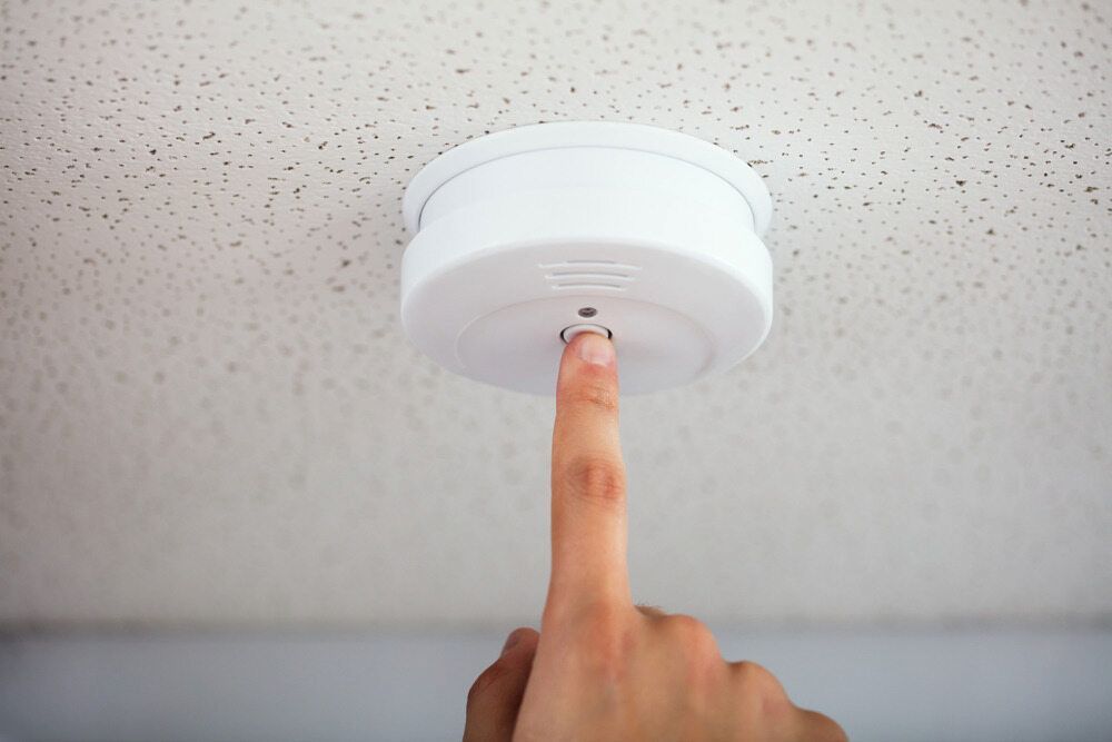 A Hand Pressing the Test Button on a White Smoke Detector — FNQ Smoke Alarms & Maintenance in Smithfield, QLD
