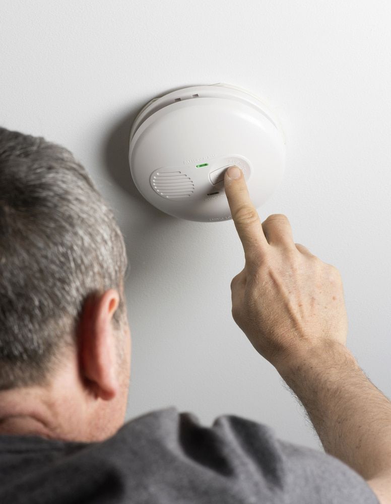 Person Testing a White Smoke Detector on a Ceiling — FNQ Smoke Alarms & Maintenance in Mareeba, QLD