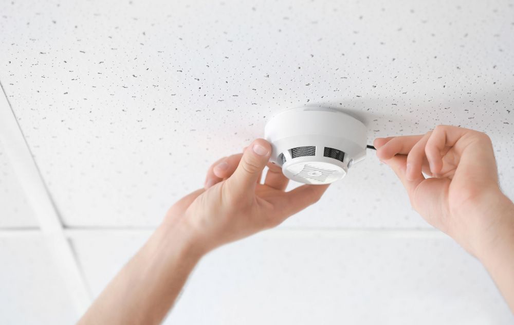 Hands Installing a White Smoke Detector on a Textured Ceiling — FNQ Smoke Alarms & Maintenance in Herberton, QLD