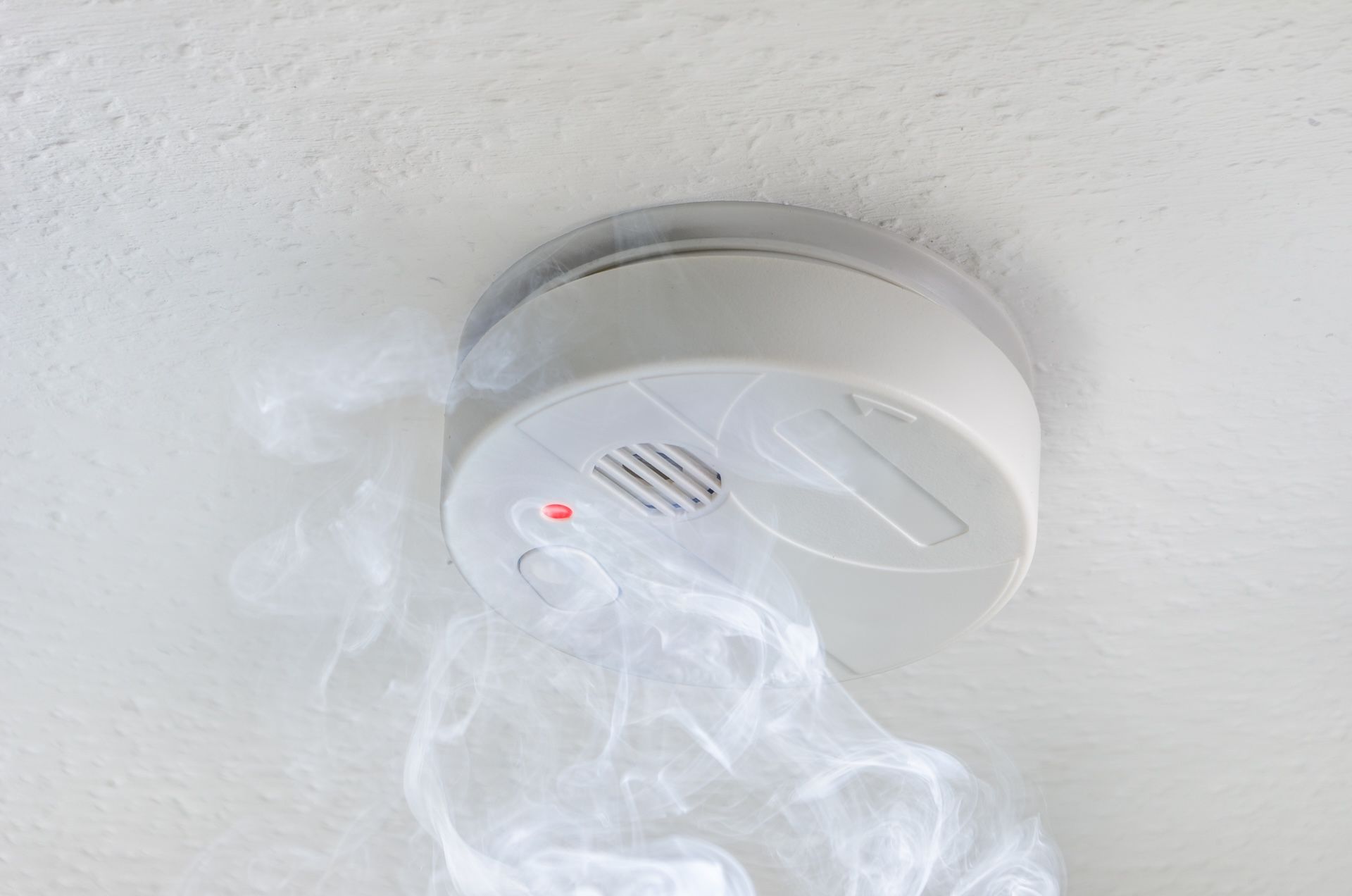 Smoke Billowing From a White Smoke Detector Mounted on a White Ceiling — FNQ Smoke Alarms & Maintenance in Innisfail, QLD