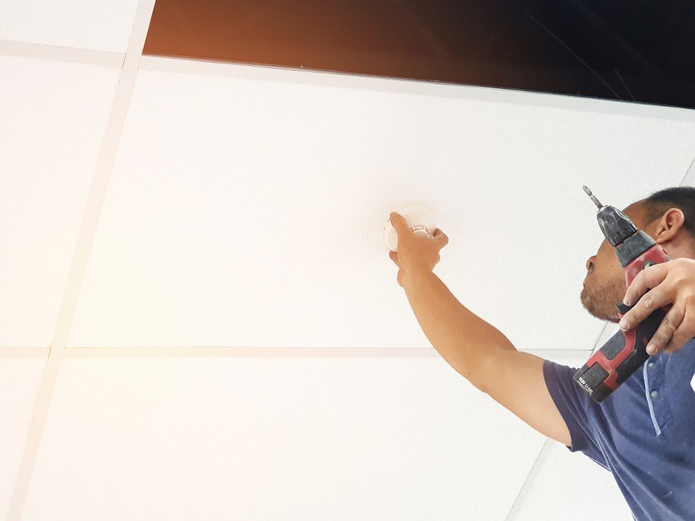 Person Installing a Device on a White Ceiling With a Power Drill — FNQ Smoke Alarms & Maintenance in Goldsborough, QLD