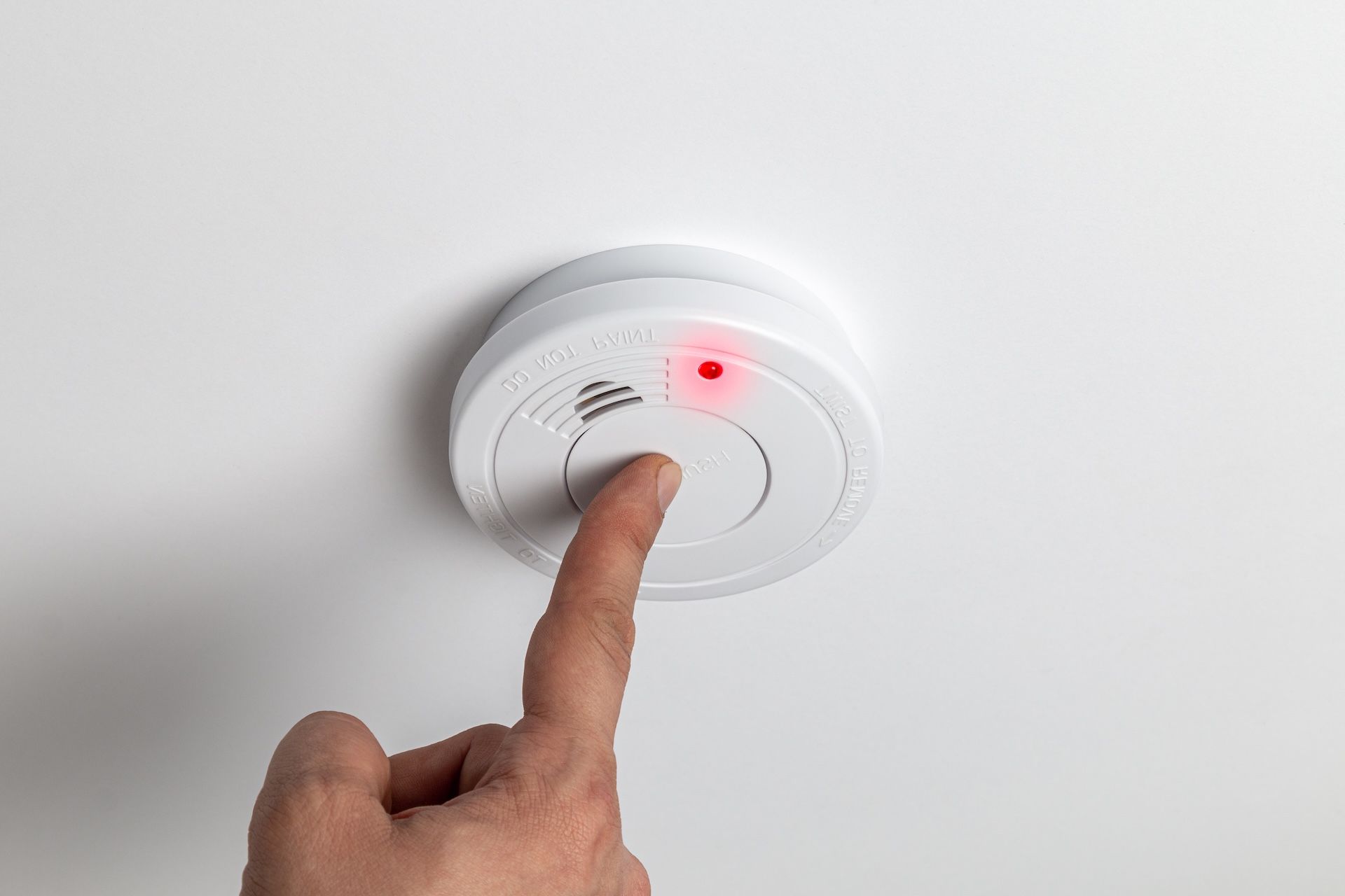 Finger Pressing the Test Button on a White Smoke Detector Mounted — FNQ Smoke Alarms & Maintenance in Herberton, QLD