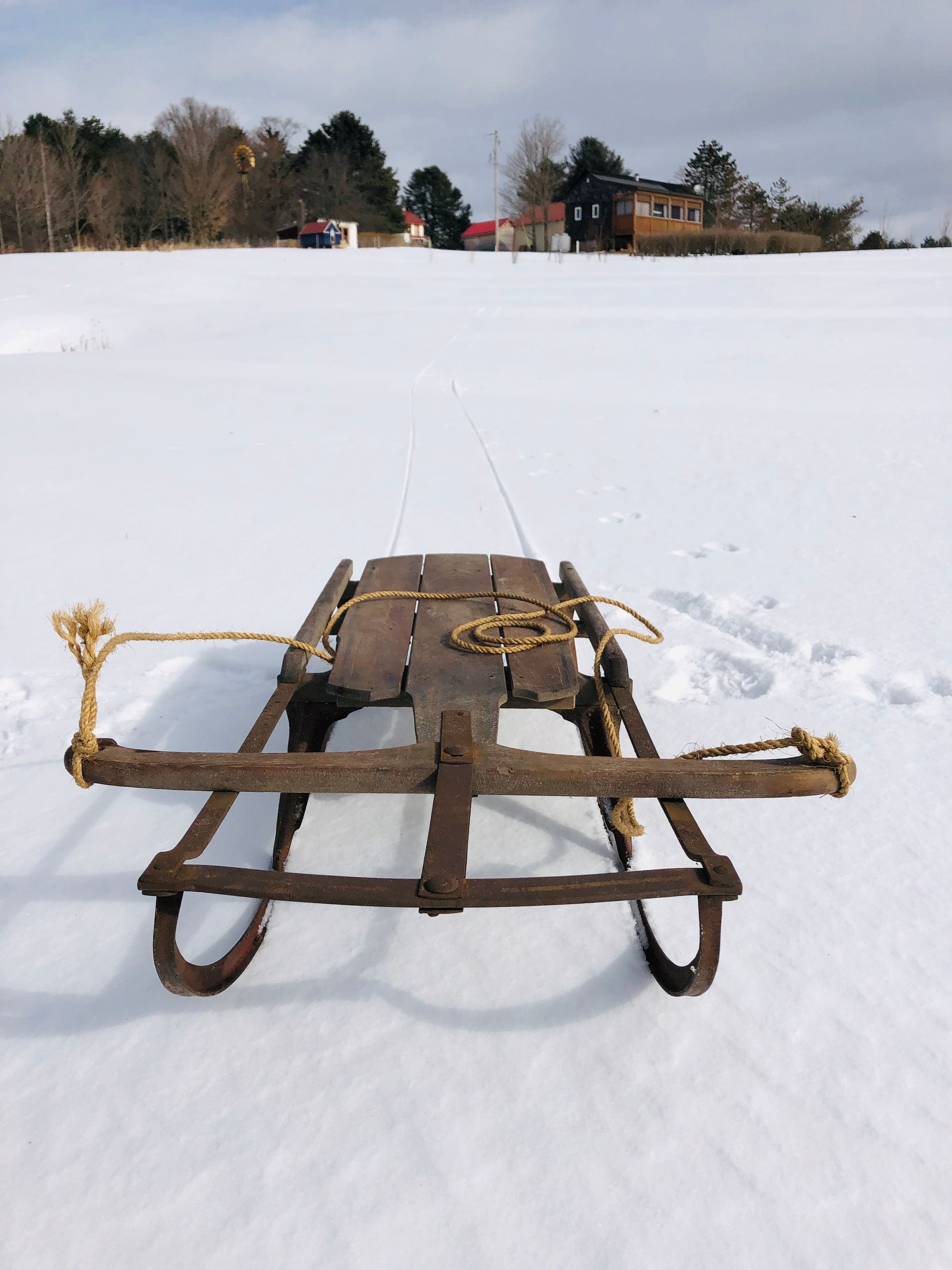 Rusty sled on a snow-covered field, with houses and trees in the background.