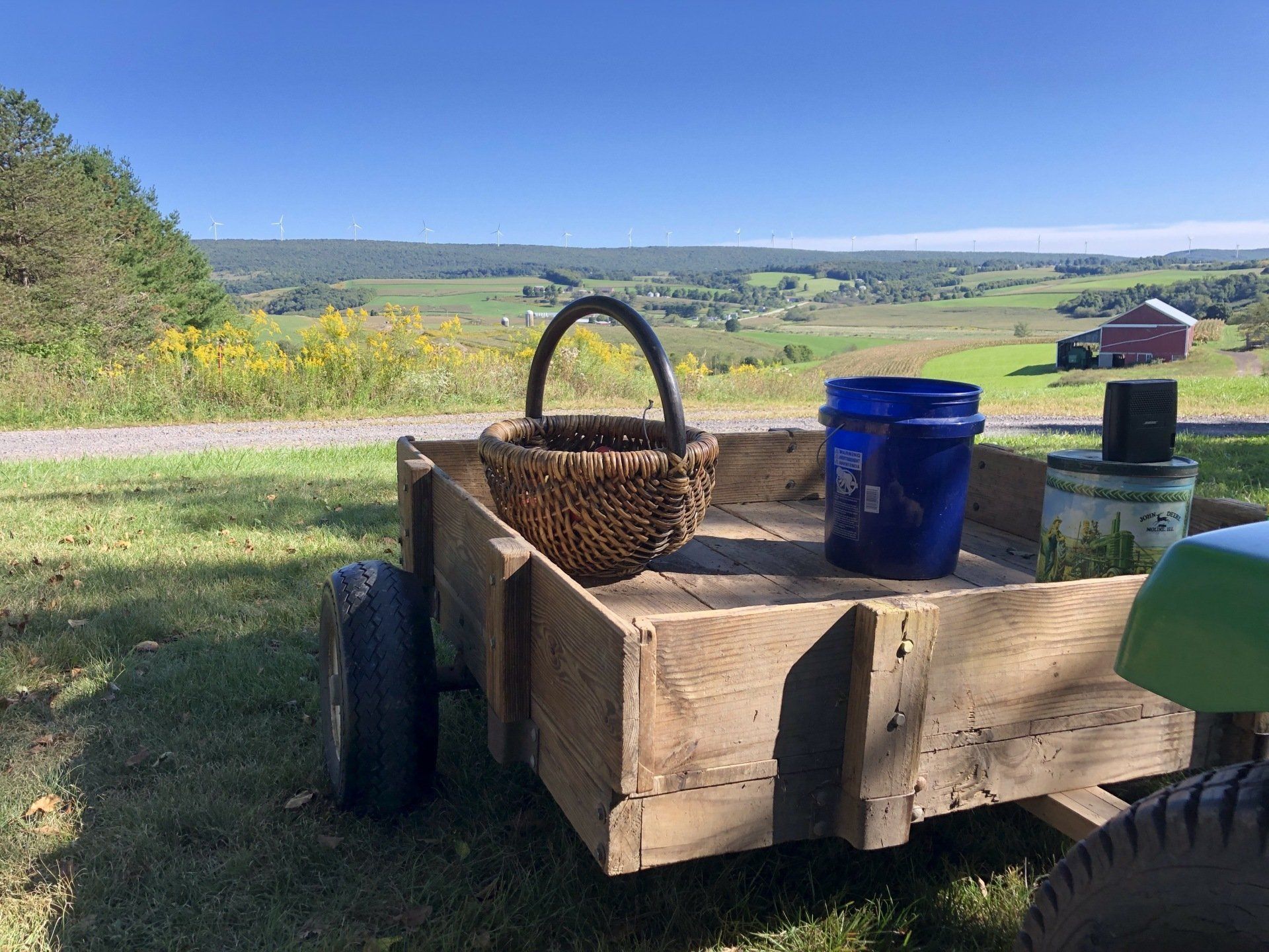 Wooden cart with basket and bucket on a sunny day in front of a rural landscape with a barn.
