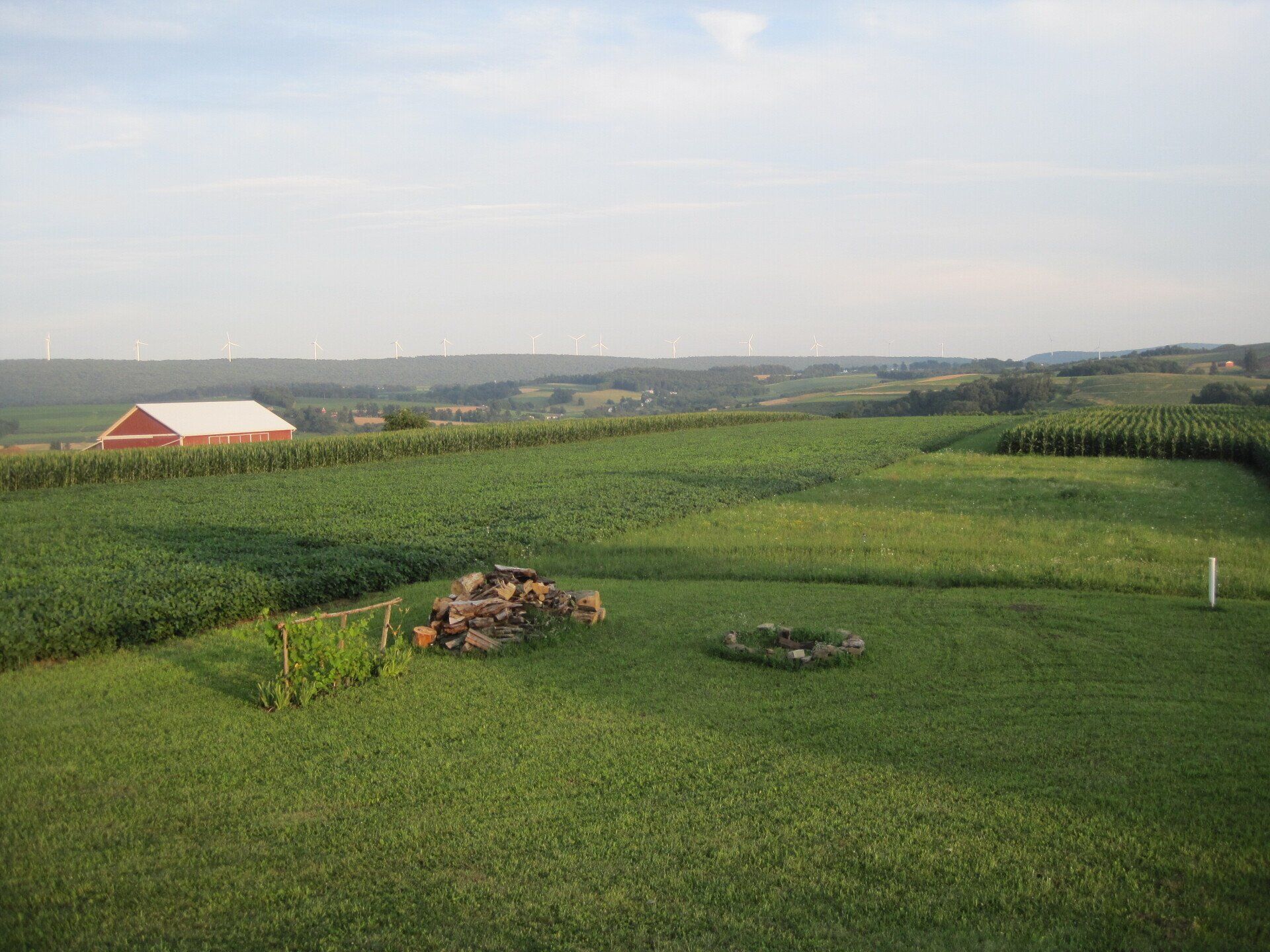 Rolling green farmland with a red barn in the distance under a hazy sky.